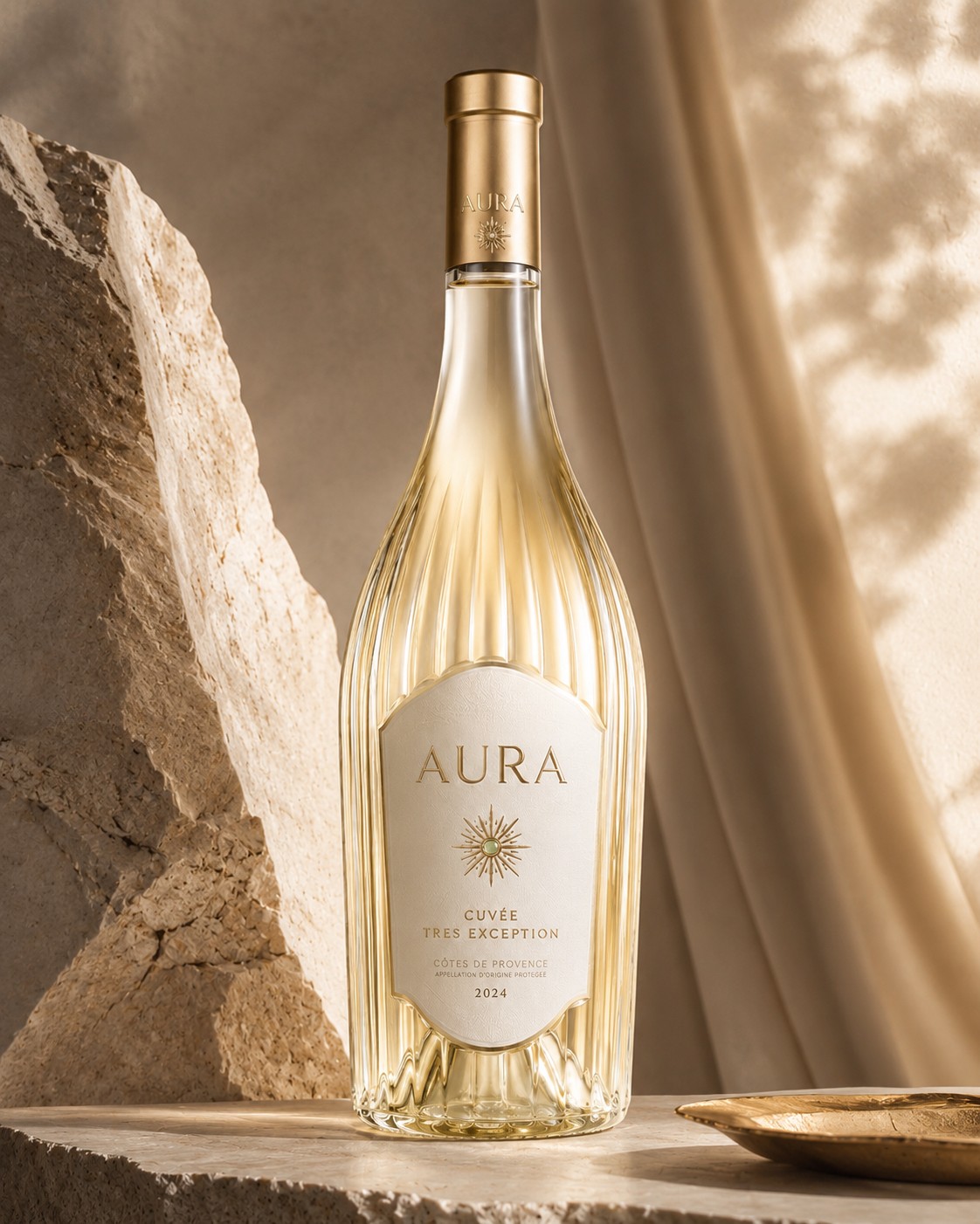 Flacon AURA TRÈS EXCEPTION blanc 2024, verrerie striée et capsule laiton, posé sur un socle de pierre calcaire drapé de lin beige